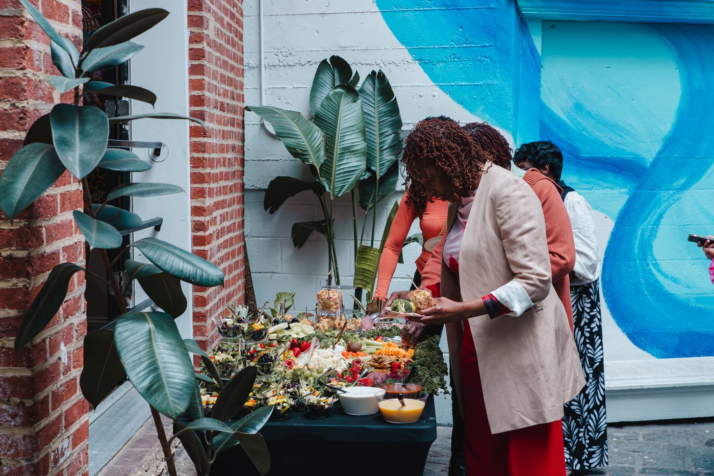 Guests serving from a grazing table against the brick and mural in the courtyard at Stem & Vine, Baltimore