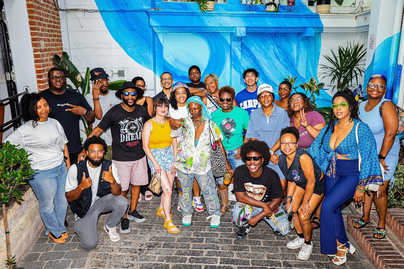 A big group photo under the blue mural in the brick courtyard during Groove House Radio at Stem & Vine, Baltimore