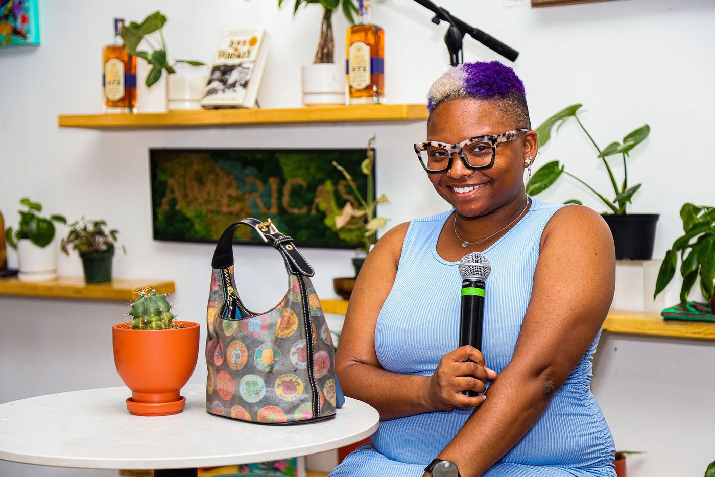 A guest speaking into a microphone in front of the plant shelves during Groove House Radio at Stem & Vine in Baltimore