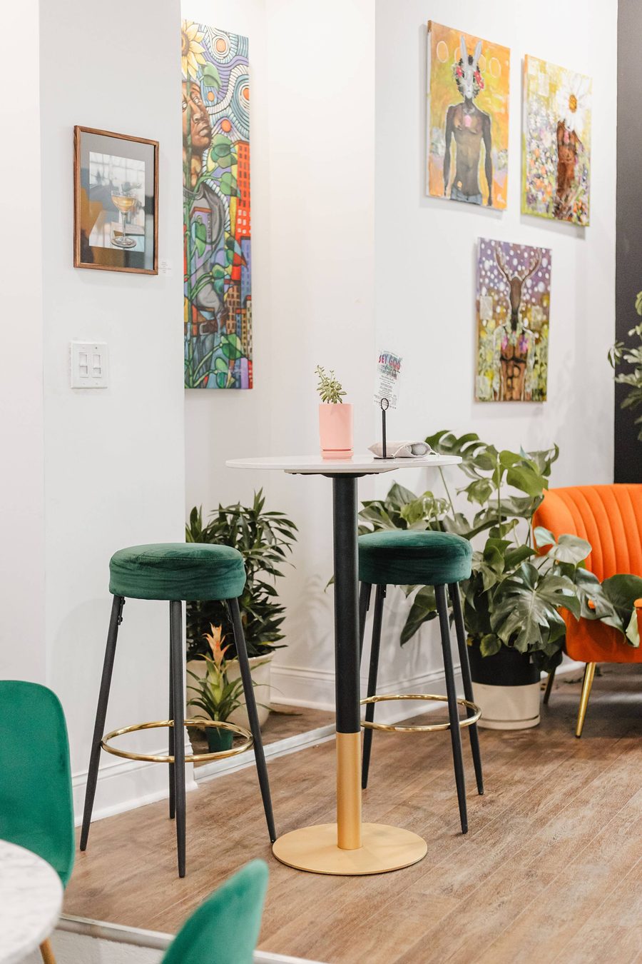 Green velvet stools at a small cafe table beneath framed paintings at Stem & Vine, Baltimore