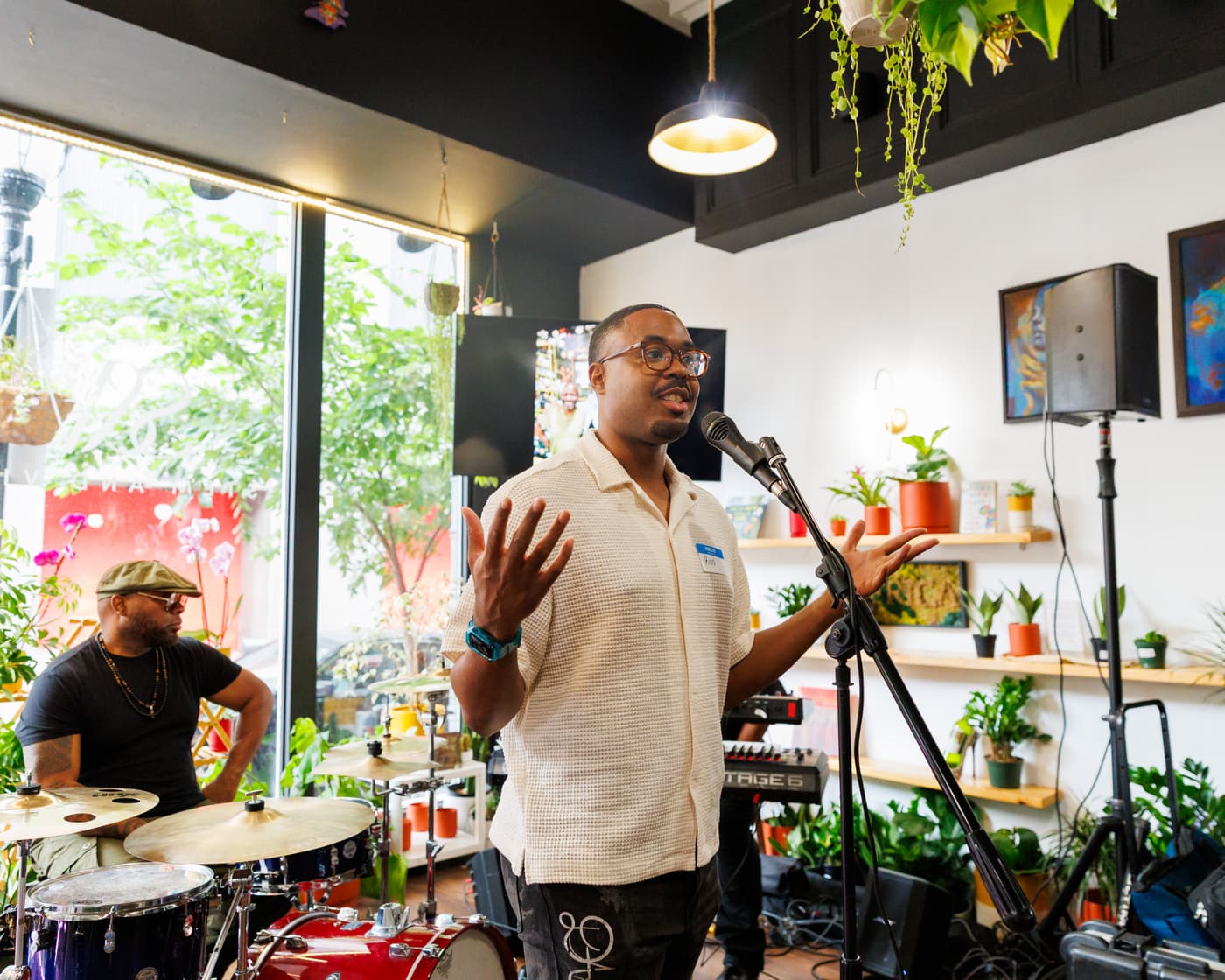Singer performing at a microphone among the plant shelves at Stem & Vine in Baltimore