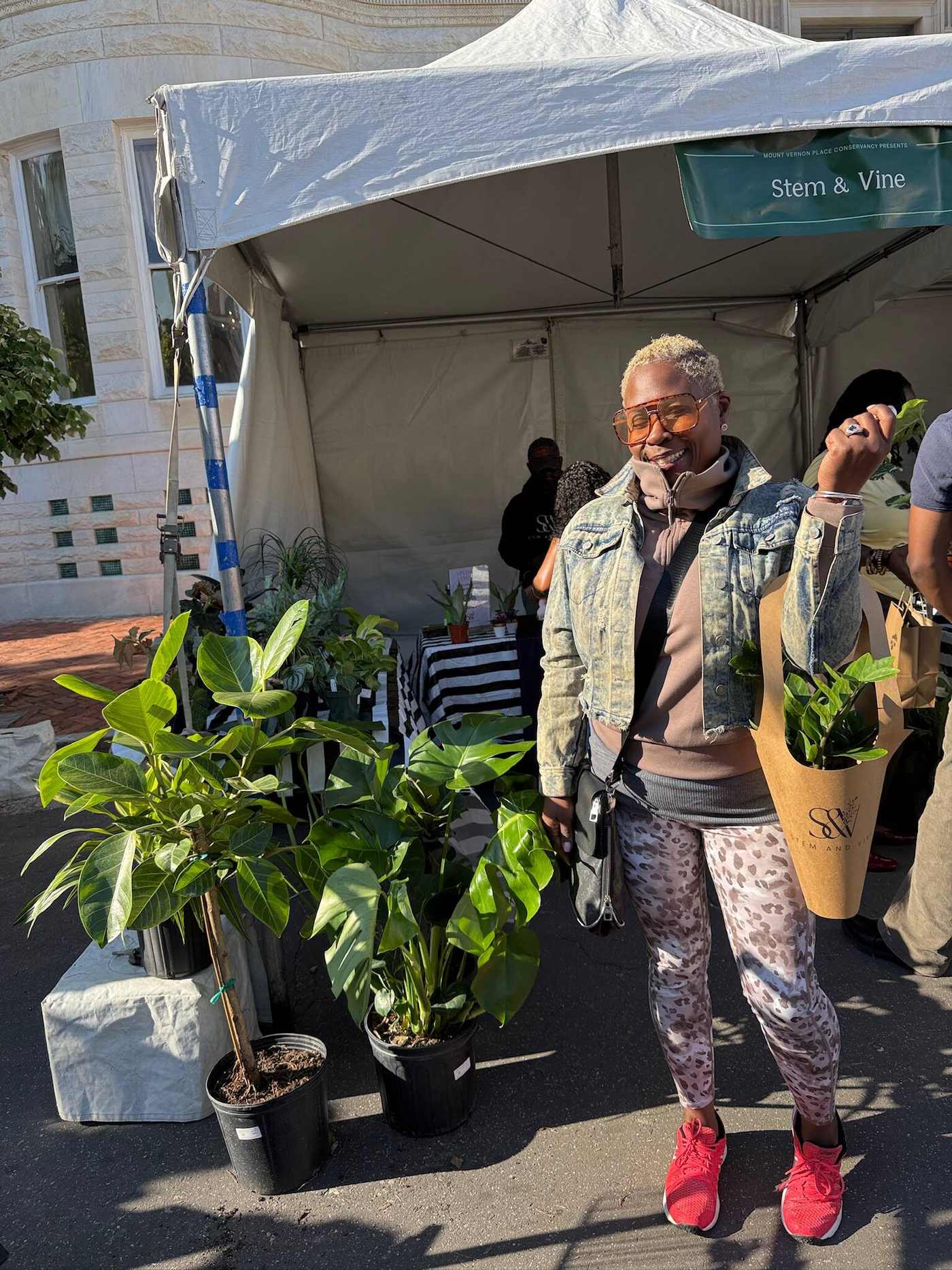 Guest smiling beside potted plants at a Stem & Vine market tent in Baltimore