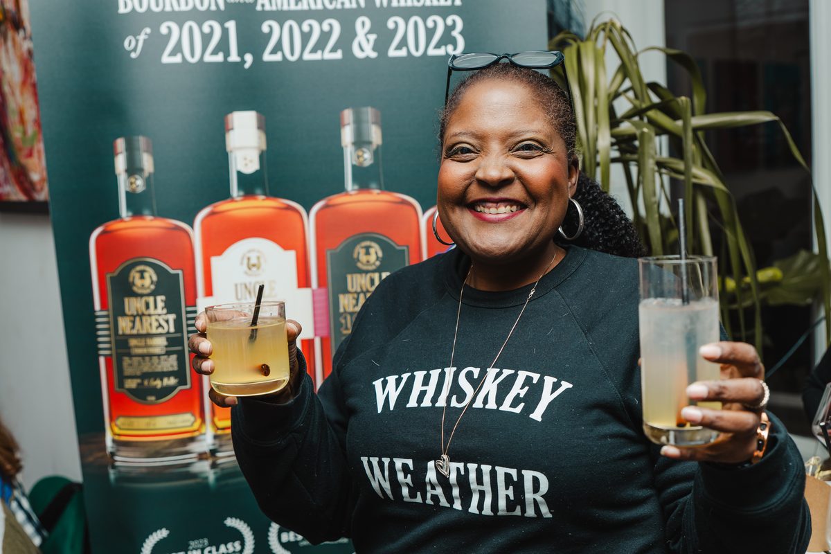 A guest smiling with Uncle Nearest bottles during a whiskey tasting at Stem & Vine in Baltimore